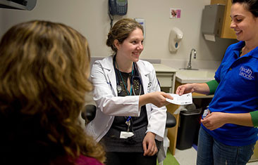 A woman in a white lab coat hands a piece of paper to a person to her left