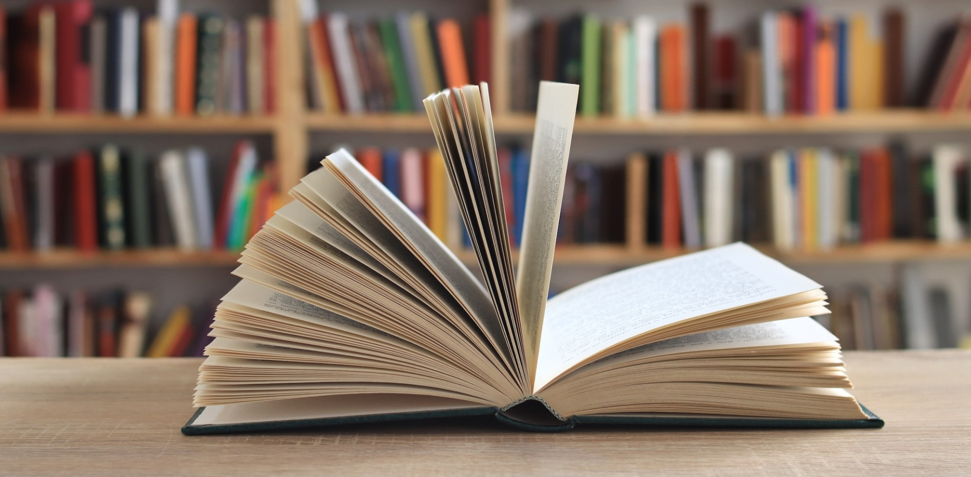 An open book in front of a bookshelf.